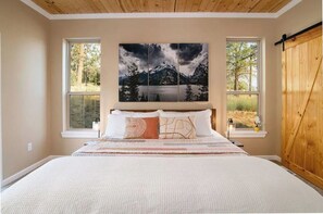 Ein Schlafzimmer mit einem großen Bett, zwei Fenstern, einer Holzbalkendecke und einem Gemälde einer Berglandschaft über dem Bett.