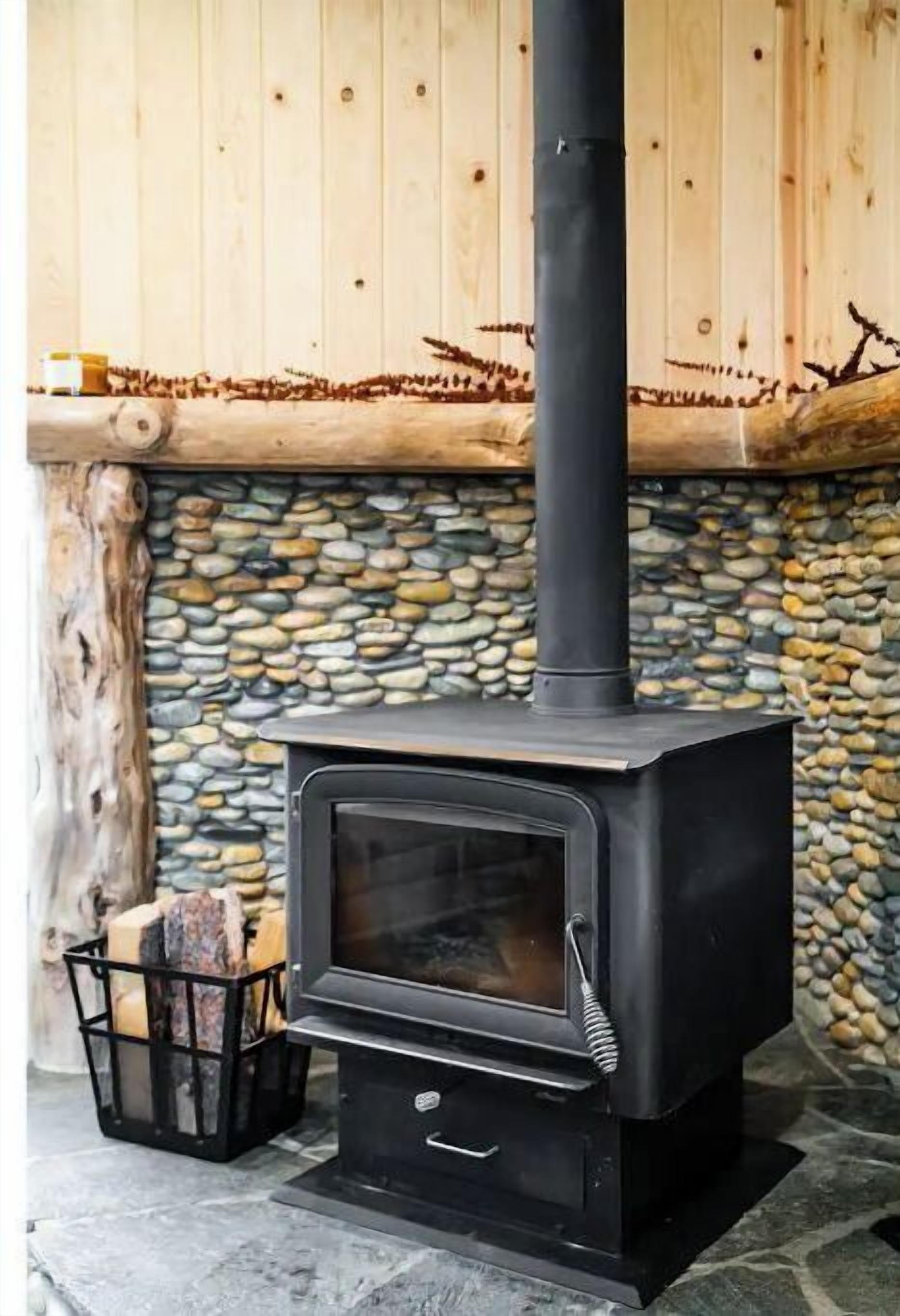 A wood-burning stove with a stone wall and wooden logs stored nearby.