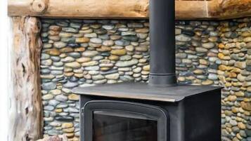 A wood-burning stove with a stone wall and wooden logs stored nearby.