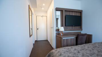 Une chambre d’hôtel comprenant un lit, un téléviseur fixé au mur, un bureau avec une lampe et une porte donnant sur une autre pièce.