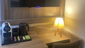 A hotel room with a flat-screen TV mounted on the wall, a coffee maker, a kettle, a lamp, and a chair. - Hotel Cataleya BV (Almere)