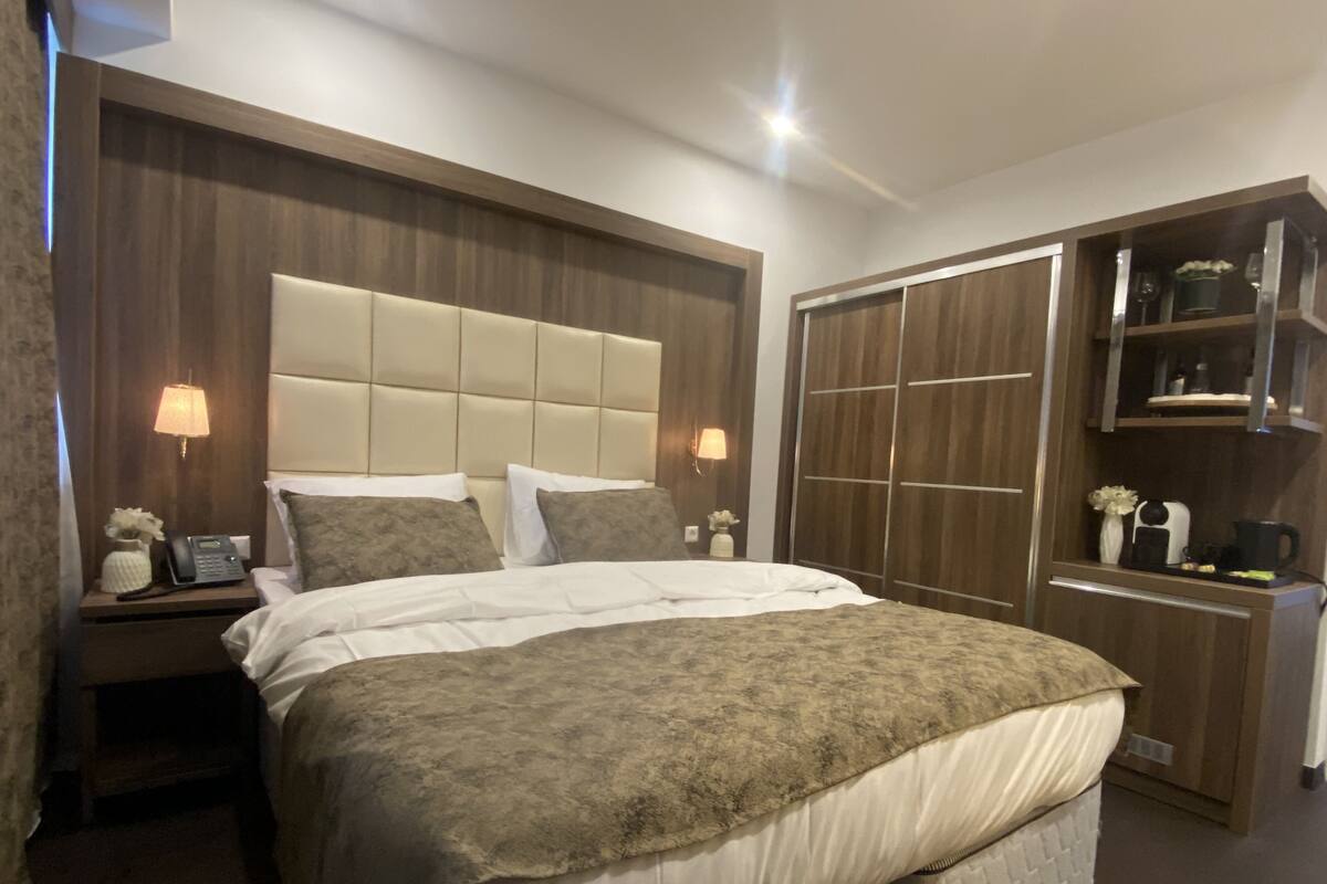 Una habitación de hotel con una cama grande, cabecera de madera, armario y lámparas de noche.