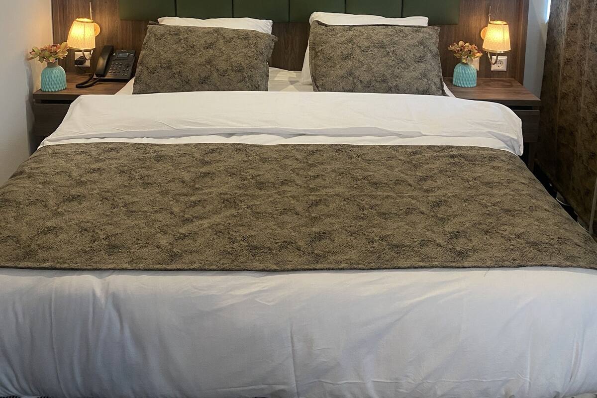 Una cama bien hecha con una colcha estampada, dos lámparas de noche, un teléfono y un florero con flores en cada mesita.