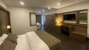 A modern hotel room with a large bed, a desk with a lamp, a TV, and a wardrobe. - Hotel Cataleya BV (Almere)