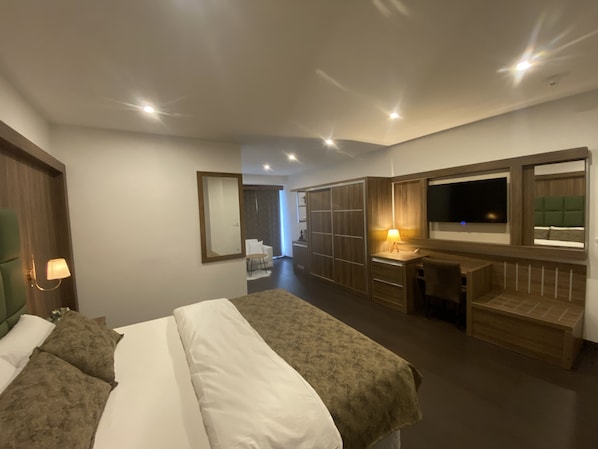 Habitación de hotel moderna con una cama grande, un escritorio con lámpara, televisión y armario.