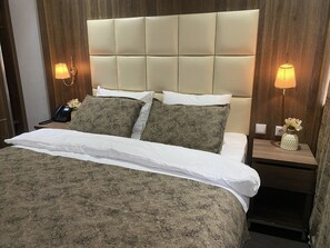 Een hotelkamer met een groot bed, twee bedlampen, een nachtkastje met een telefoon en een bloemetjesvaas.