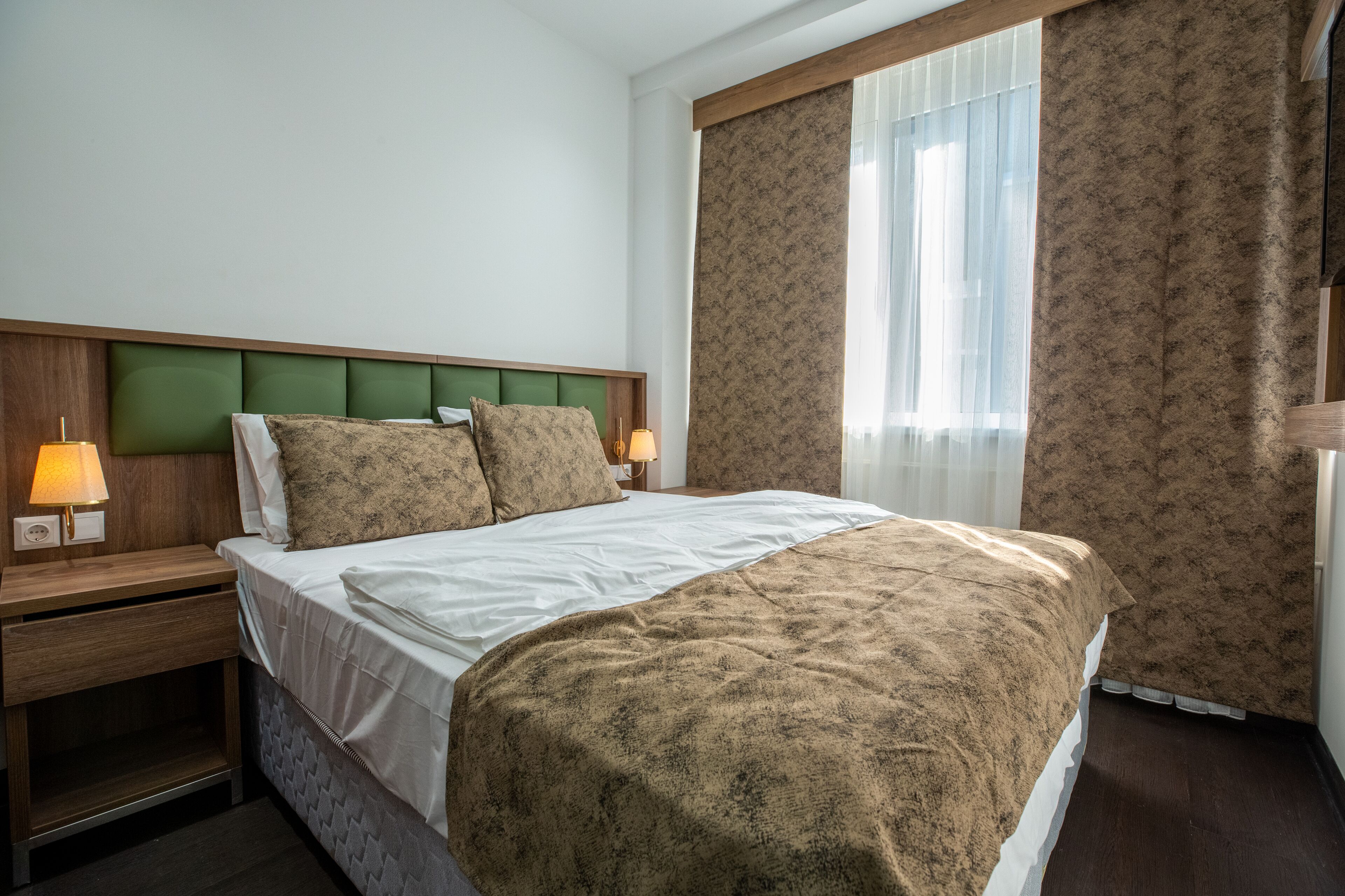 Una habitación de hotel con cama, mesitas de noche, lámparas y una ventana con cortinas.