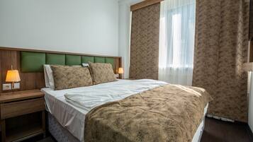Una habitación de hotel con cama, mesitas de noche, lámparas y una ventana con cortinas.
