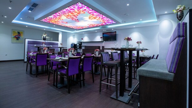 A modern dining area with purple chairs and tables, a ceiling with a colorful light display, and a flat-screen TV mounted on the wall. - Hotel Cataleya BV (Almere)