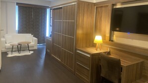 A modern room with a sofa, a small round table, a desk with a lamp, and a large flat-screen TV. - Hotel Cataleya BV (Almere)