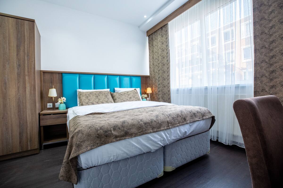 Una habitación de hotel con cama, mesitas de noche, armario y ventana con cortinas.