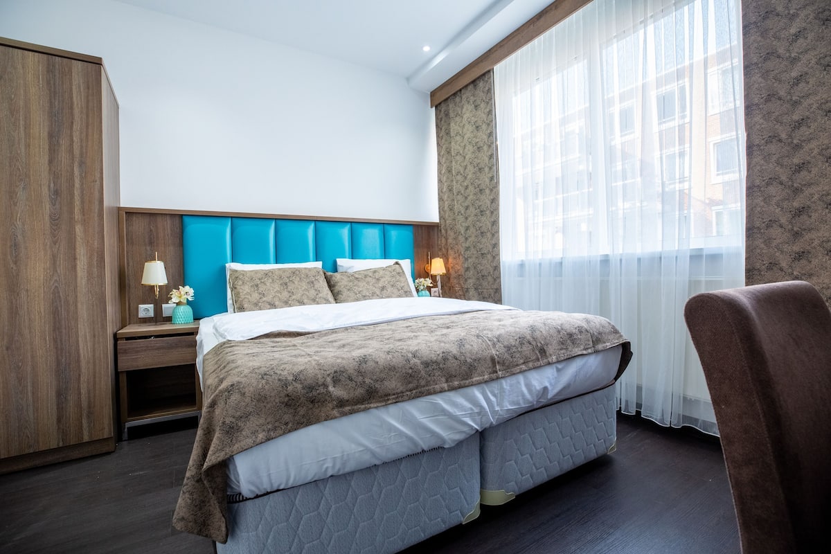Une chambre d’hôtel avec un lit, des tables de chevet, une armoire et une fenêtre avec des rideaux.