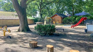Un parque infantil con un tobogán, columpios y una pequeña construcción de madera.