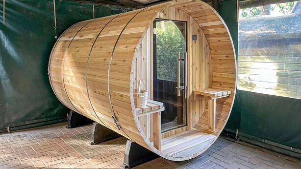 Una sauna de madera con exterior curvo, una puerta de cristal y un banco pequeño en el interior.