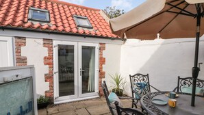 A courtyard with a tiled roof, a glass door, a table with chairs, and a sign that reads "Bluebell Cottage". - Bluebell Cottage (Bridlington)