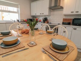 Cozinha moderna com armários brancos, mesa de jantar redonda posta com tigelas, pratos e talheres, e um vaso com flores.