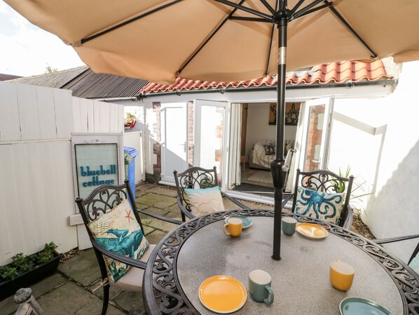 A patio with a round table, chairs, and an umbrella. There is a sign that reads "bluebell cottage."