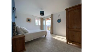 A bedroom with a bed, a wooden wardrobe, a ceiling light, and a view through an open door. - Bwa Flote' (Les Trois-Îlets)