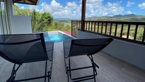 A balcony with a pool, two lounge chairs, and a view of mountains and greenery. - Bwa Flote' (Les Trois-Îlets)