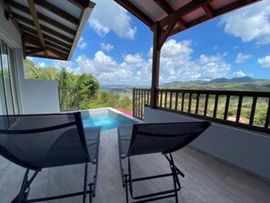 A balcony with a pool, two lounge chairs, and a view of mountains and greenery.