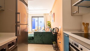 A compact kitchen with a built-in refrigerator, a coffee machine, and a small dining area with a green sofa. - Majorelle - Daily rental Casablanca (Casablanca)