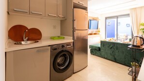 Eine kleine Küche mit Waschmaschine, Kühlschrank und Essbereich mit einem grünen Sofa.