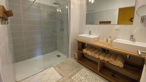 Ein modernes Badezimmer mit einer Duschkabine aus Glas, zwei Waschbecken und einem Holz-Waschtisch mit Handtüchern.