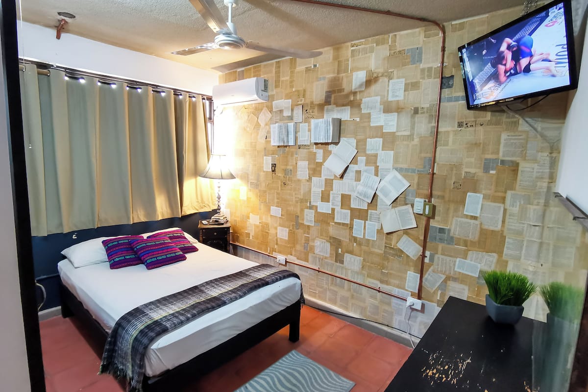 Una habitación de hotel con una cama, un escritorio, un televisor y una pared cubierta de papeles.