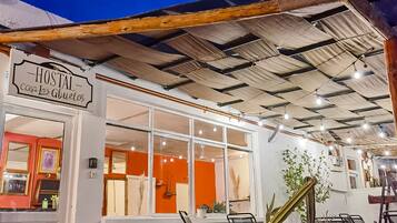 Un hostal acogedor llamado 'Hostal Casa los Abuelos', con un techo de madera rústica, ventanas amplias y diversas plantas en macetas.