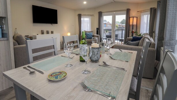 Un coin repas avec une table dressée pour quatre personnes, un téléviseur à écran plat fixé au mur et un balcon avec vue.