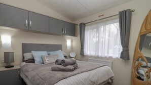 Une chambre à coucher avec un lit, des armoires grises, une table de chevet avec une lampe, une fenêtre avec des rideaux et une chaise en bois.