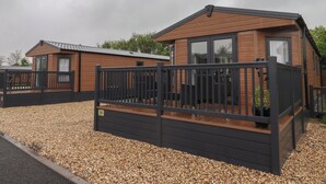 Une maison mobile en bois dotée d’une terrasse clôturée et d’une allée en gravier.