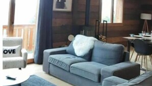 Una sala de estar acogedora con un sofá gris, una pequeña mesa redonda y un techo con vigas de madera a la vista y lámparas colgantes.