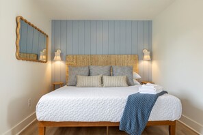 A neatly made bed with a white quilt, a blue blanket, and several pillows. There are two wall-mounted lamps on either side of the bed. - Steps to Beach · Pet Friendly · Newly Renovated (Carolina Beach)