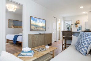 A modern living room with a sofa, a coffee table, a bed, a wooden cabinet, and a painting of a beach scene. - Steps to Beach · Pet Friendly · Newly Renovated (Carolina Beach)