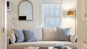 Ein Wohnzimmer mit Sofa, Couchtisch, Lampe, Spiegel und Fenster.