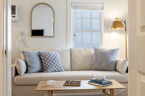 A living room with a sofa, a coffee table, a lamp, a mirror, and a window.