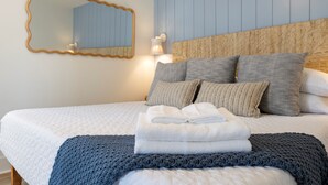 Ein ordentlich bezogenes Bett mit Kissen, einem gefalteten Handtuch und einer gestrickten Decke.