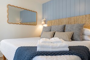 Ein ordentlich bezogenes Bett mit Kissen, einem gefalteten Handtuch und einer gestrickten Decke.