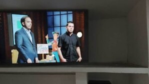 Een televisiescherm waarop een scène te zien is met twee personen, één in een pak en de ander in vrijetijdskleding, met een bord waarop staat: 'Binnenkort beschikbaar'.