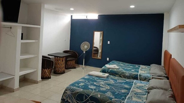 Een kamer met twee bedden, een bureau, een stoel, een ventilator en een plafondventilator.