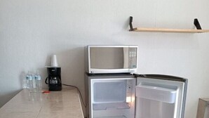 Een compacte keuken met een magnetron en koelkast, een eettafel met stoelen en een koffiezetapparaat.