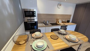 A modern kitchen with a microwave, oven, and sink. There is a dining table set with plates, bowls, and cutlery. - Welcome to the Gardens of Qiara.<br>Charming cottages in the heart of the Vosges Mo (Mattaincourt)