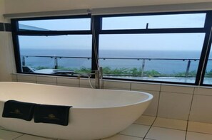 Een moderne badkamer met een vrijstaand bad, een groot raam met uitzicht op zee, en een balkon.