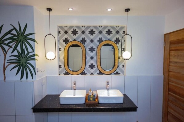 Een badkamer met twee wasbakken, een spiegel met een achterwand van geometrische tegels, en hanglampen.