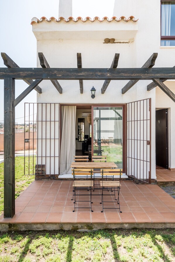 A covered patio with a wooden bench and a view of the interior through a glass door.