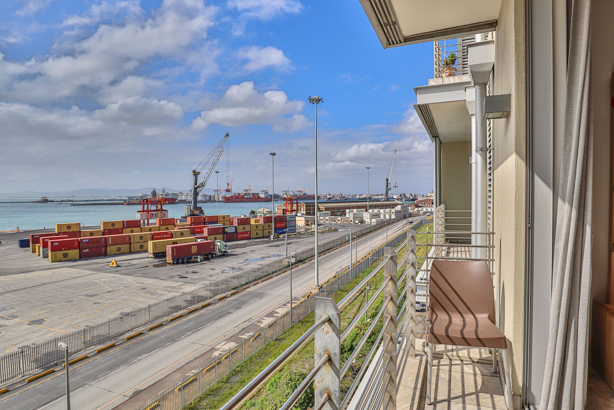 A port with shipping containers, cranes, and a clear sky.
