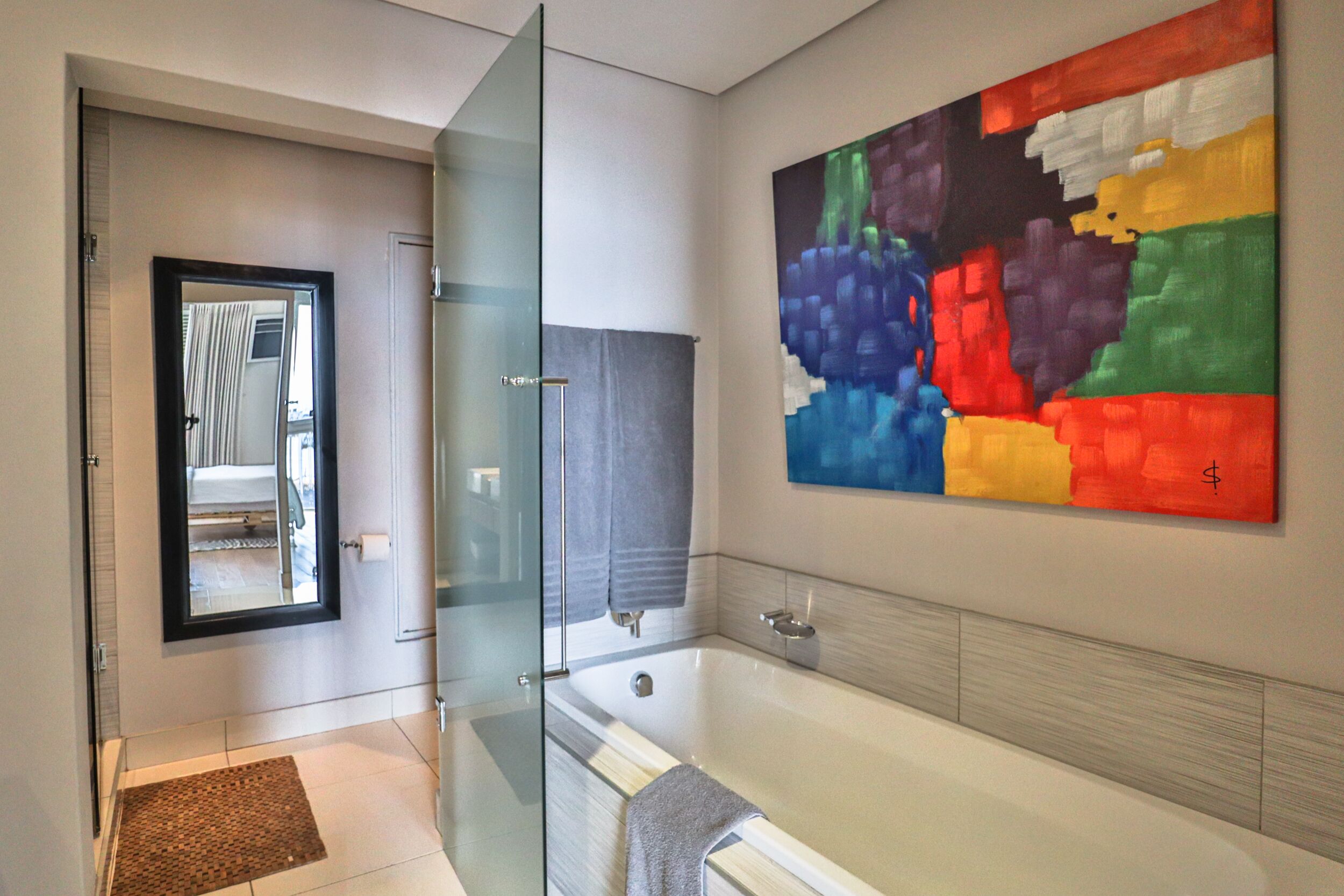 A modern bathroom with a glass shower enclosure, a large bathtub, and a colorful abstract painting on the wall.