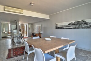 A spacious dining area with a wooden table and white chairs, a red patterned rug, and a large landscape painting on the wall. - Harbour Bridge 417 by CTHA (Cape Town)
