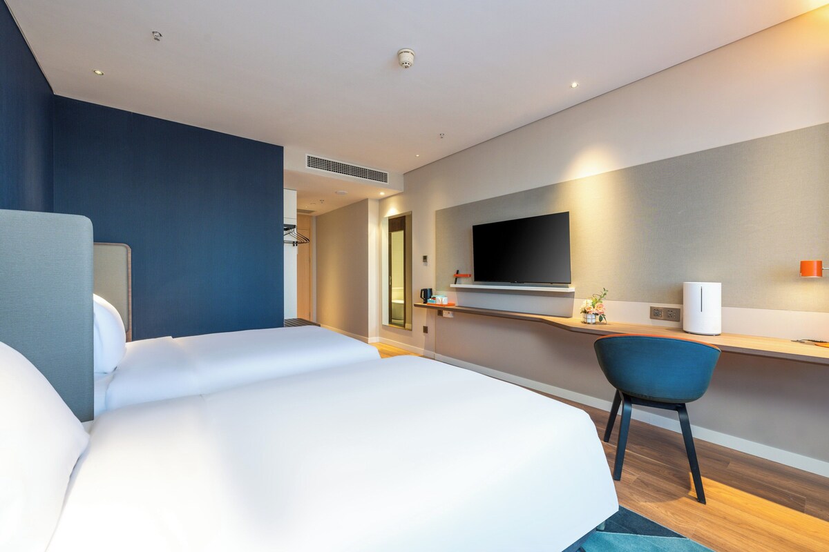 A modern hotel room with a large bed, a desk with a flat-screen TV, and a chair.